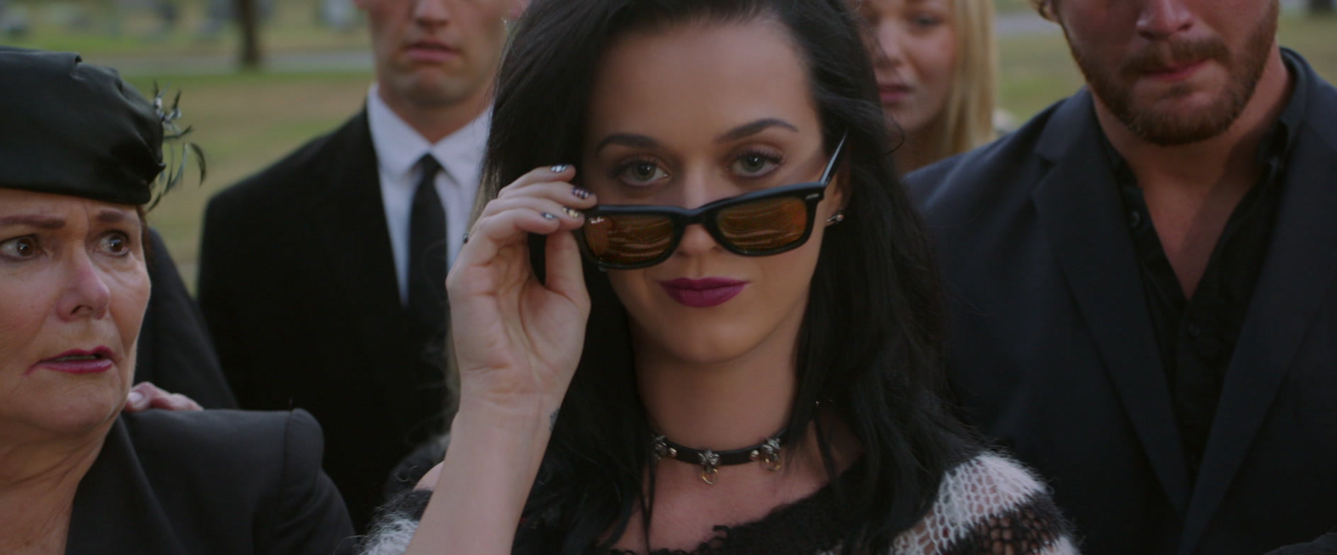 Katy Perry lowering her sunglasses at a graveside, from a music video